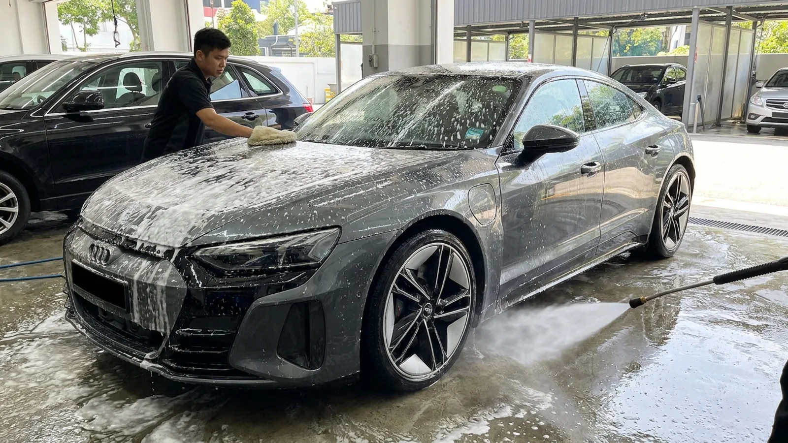 A car being hand washed with thick white foam and a soft mitt at a bright Singapore wash bay, water beading on glossy paintwork