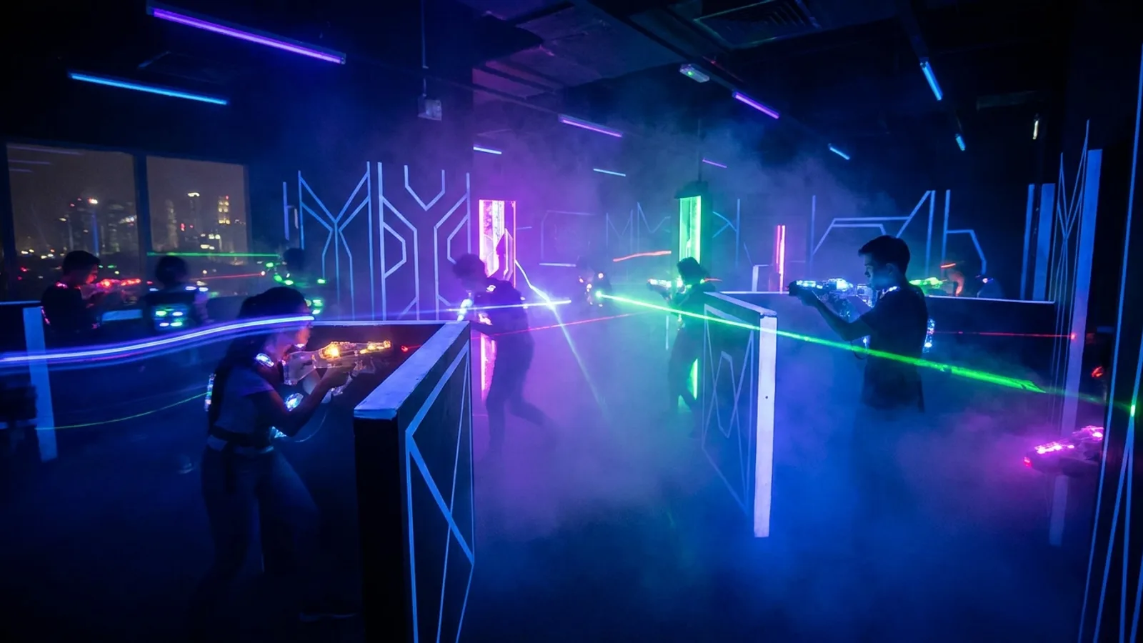 Players in a dark neon-lit indoor laser tag arena in Singapore with glowing vests and laser guns amid fog and coloured lights