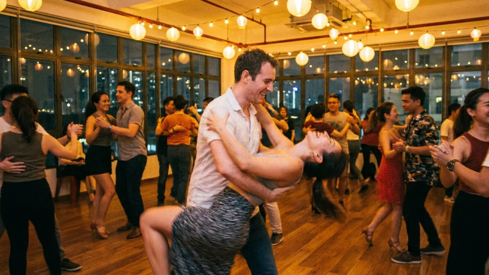 A couple social dancing salsa together on a busy dance floor in a warmly lit Singapore Latin dance studio, surrounded by other partner dancers
