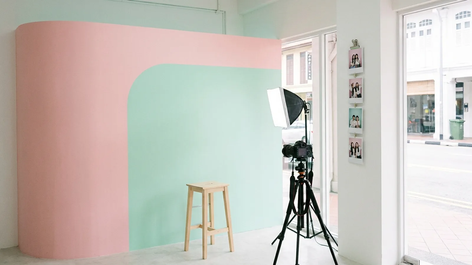 A bright self photo studio in Singapore with a remote-controlled camera, a stool and a clean backdrop, with printed photo strips