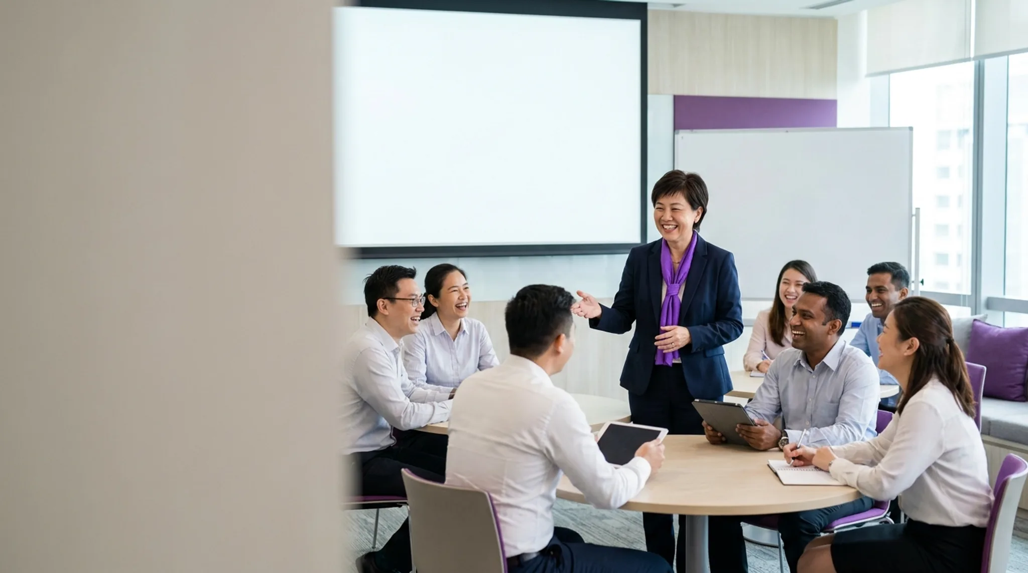 Corporate trainer leading a workshop in a Singapore training room, with a laptop showing course enrolment search results