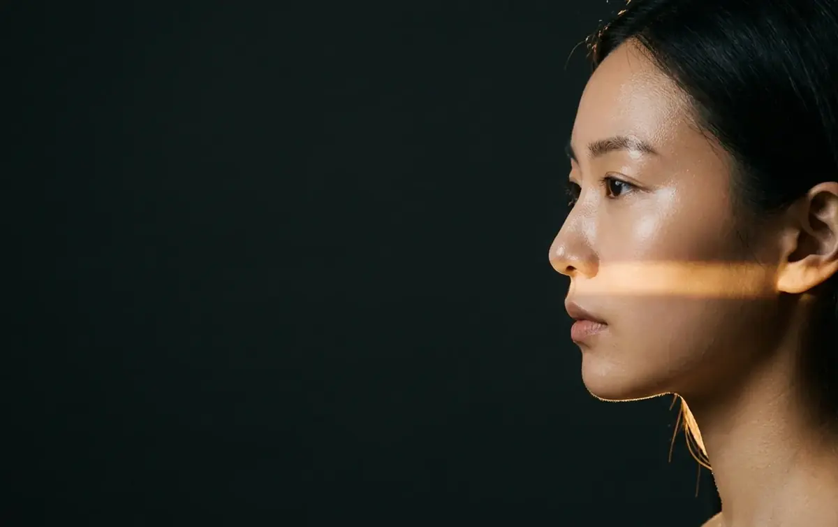 Profile of a woman against near-black, a single narrow blade of warm light across her cheekbone