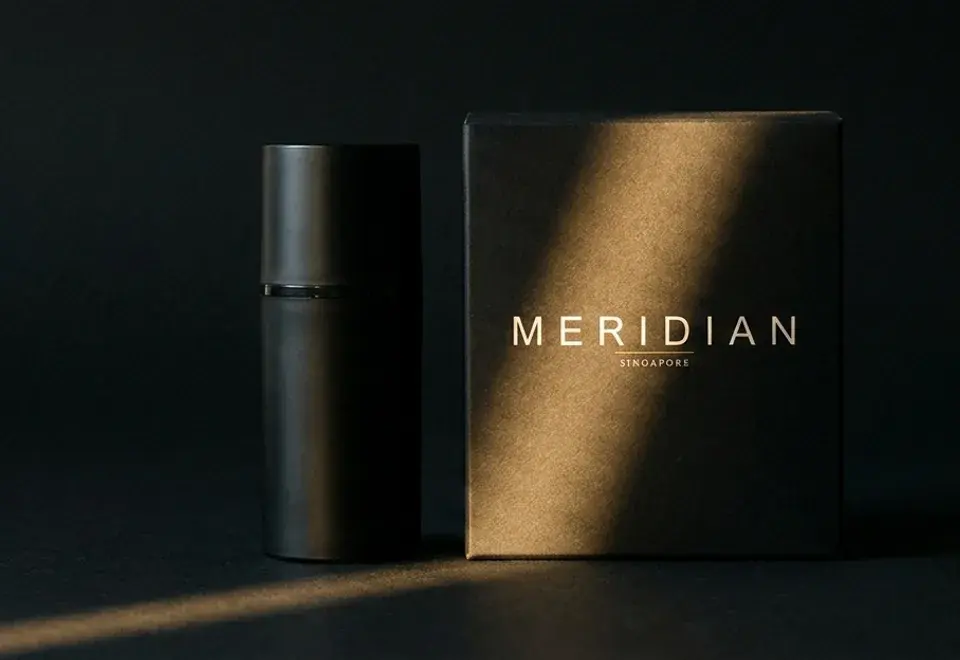 Matte black Meridian carton beside a dark glass jar, lit by one warm highlight