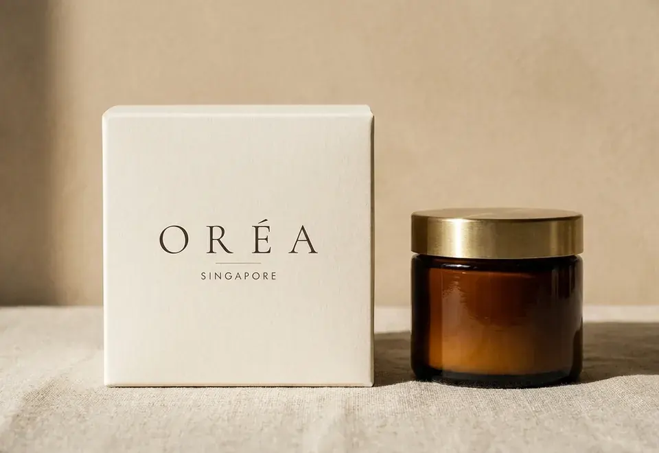 Cream Oréa carton beside an amber glass jar with a brushed brass lid