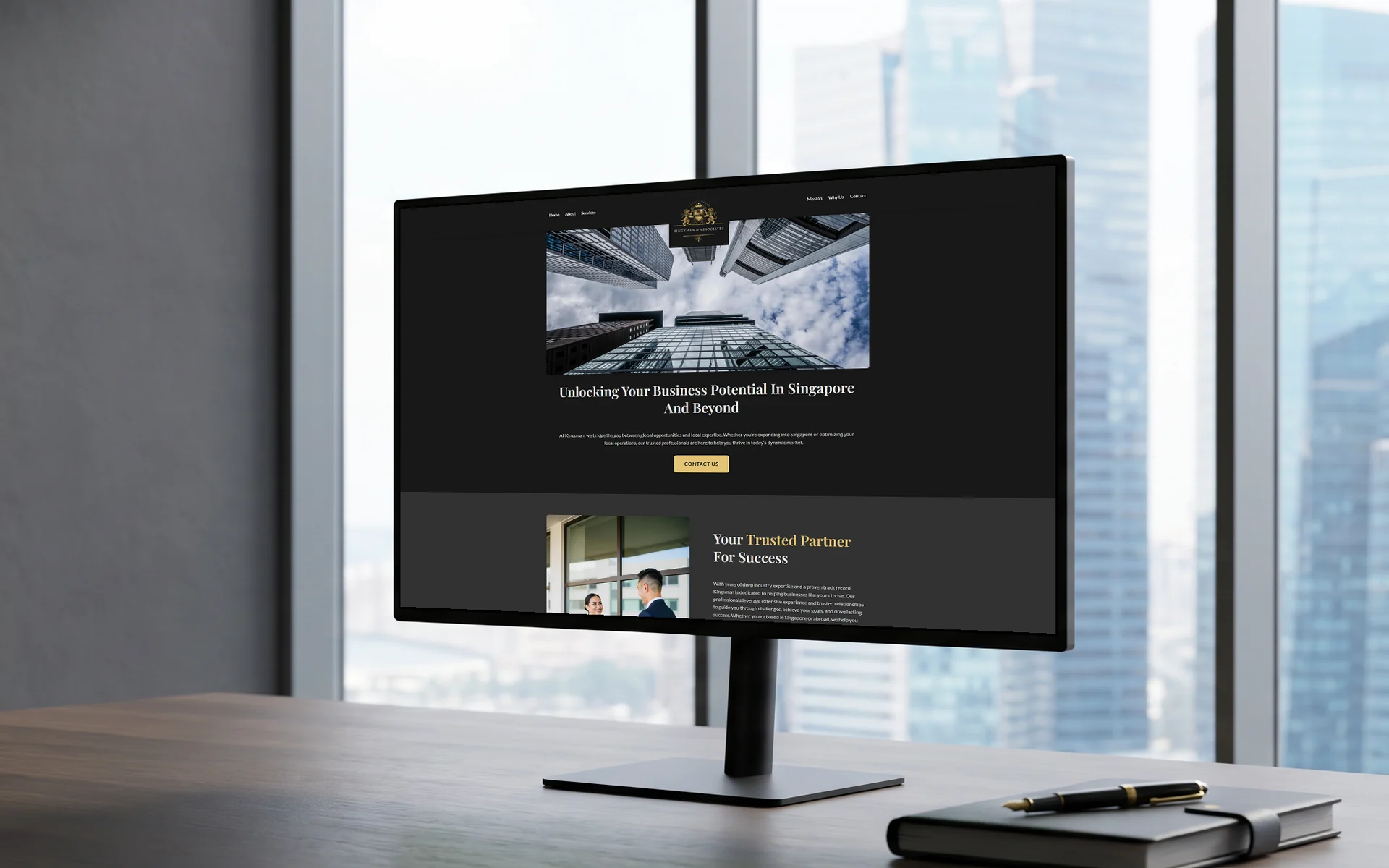 Kingsman & Associates homepage, "Unlocking Your Business Potential In Singapore And Beyond" under its gold crest, on a 27-inch monitor on a dark oak desk in a bright corner office, city towers through floor-to-ceiling windows, a leather notebook and pen beside it