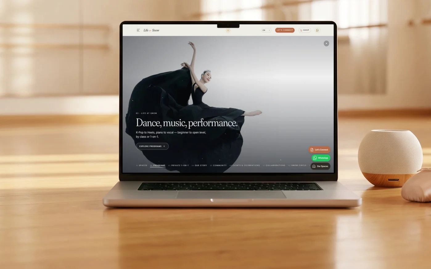 Life at Snow homepage, "Dance, music, performance." over a dancer in a flowing black gown, on a laptop on a polished wooden dance studio floor before a mirrored wall and ballet barre, with pink ballet shoes and a small speaker beside it in soft morning light