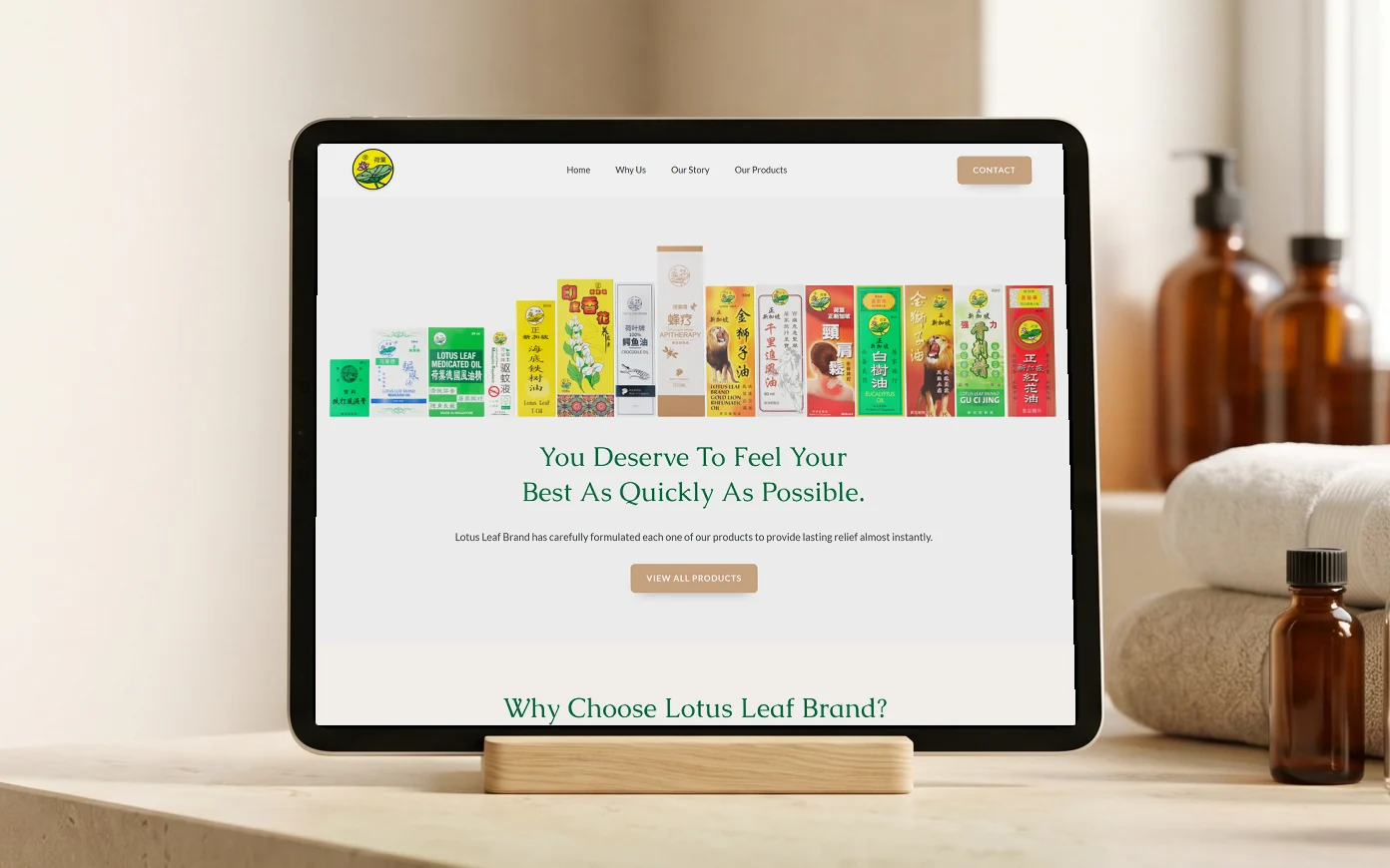 Lotus Leaf Brand homepage, "You Deserve To Feel Your Best As Quickly As Possible." under the row of product boxes, on a tablet on a limestone bathroom vanity with folded cotton towels, amber glass bottles and river stones, in soft daylight