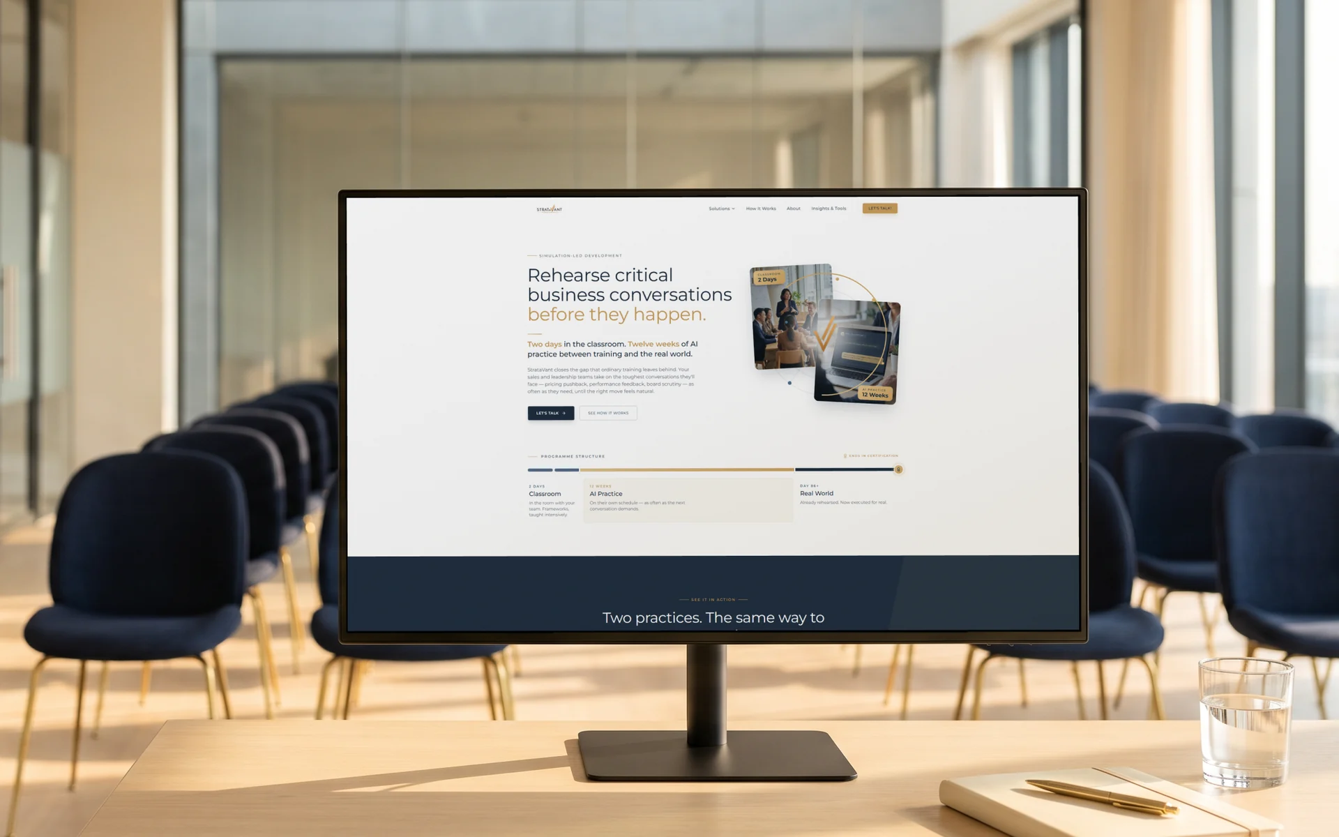 StrataVant homepage, "Rehearse critical business conversations before they happen." on cream with navy and gold, on a 27-inch monitor at the front of a sunlit training room with rows of empty navy chairs