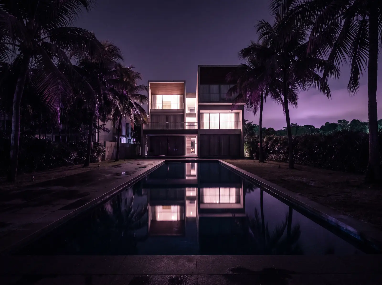 A modern Singapore cluster house at night behind a long still pool, palms dark against a violet sky